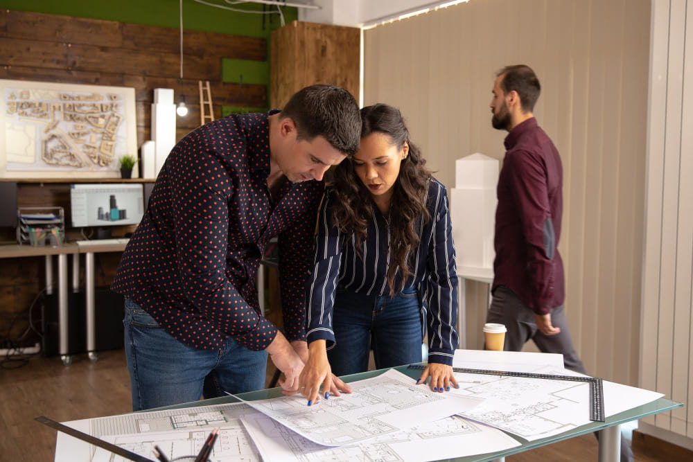 Dos técnicos revisando los planos de un proyecto de edificación en el estudio