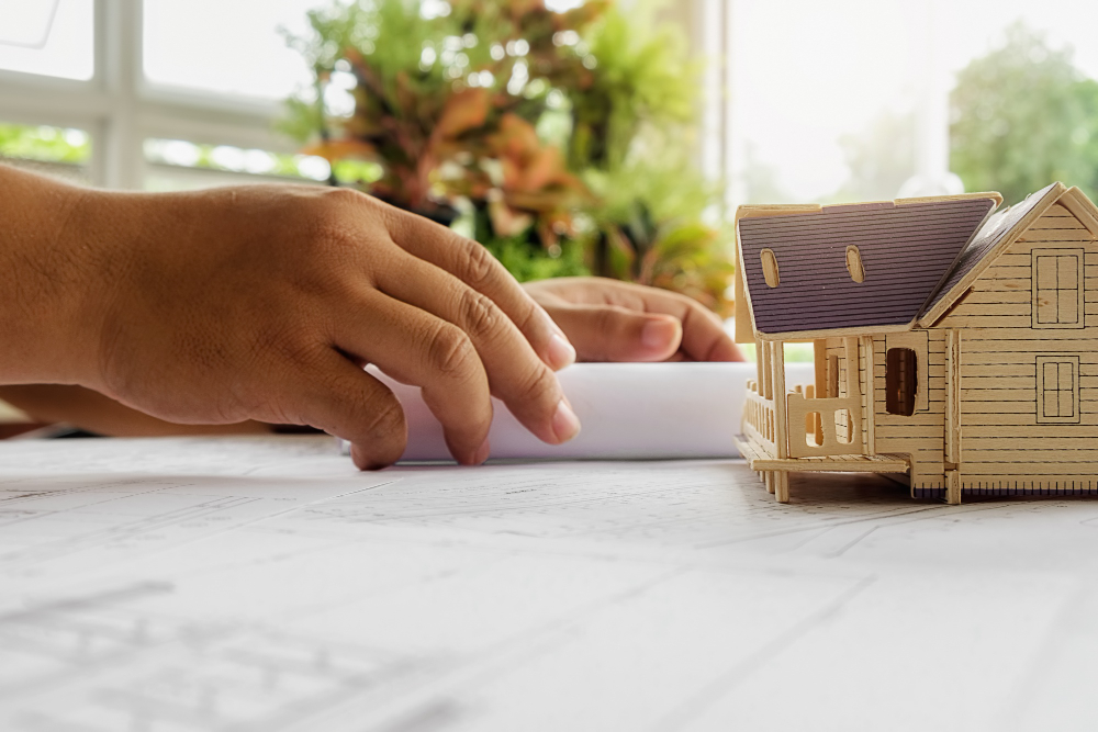 Manos de un técnico junto a una maqueta de madera de una vivienda sobre los planos del proyecto