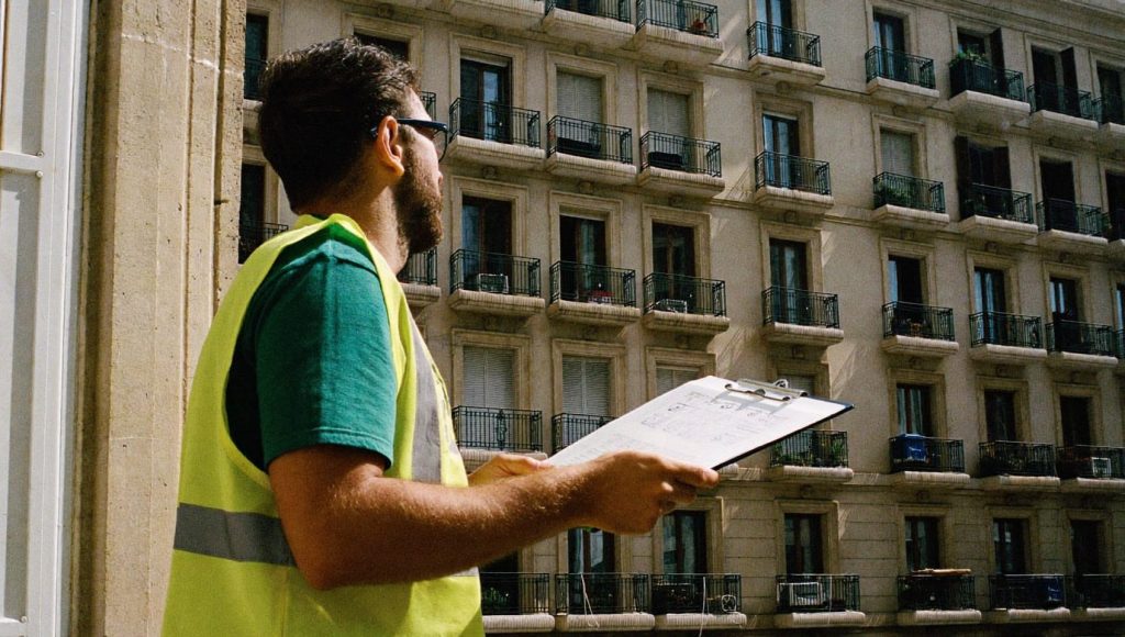 Técnico de edificación con casco y carpeta examinando la fachada de un edificio residencial clásico en Madrid