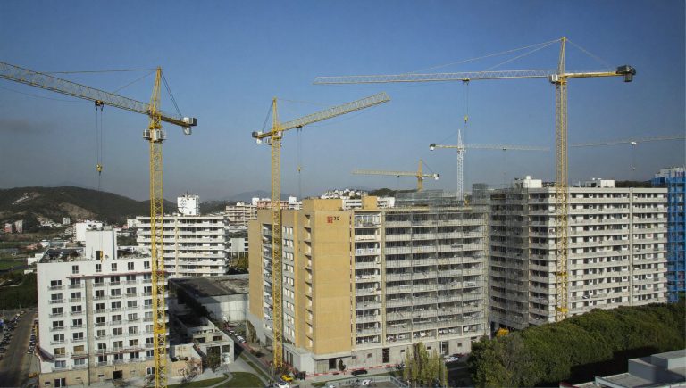 Panorámica de un barrio residencial en construcción con grúas torre y bloques con andamios