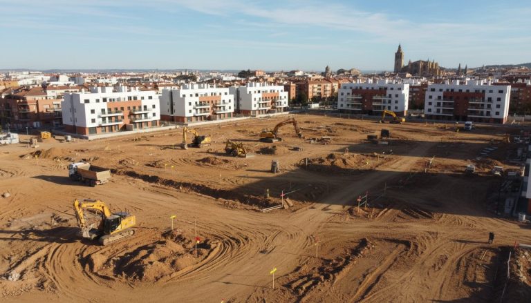 Vista elevada de una parcela en desarrollo con maquinaria de movimiento de tierras y bloques residenciales al fondo